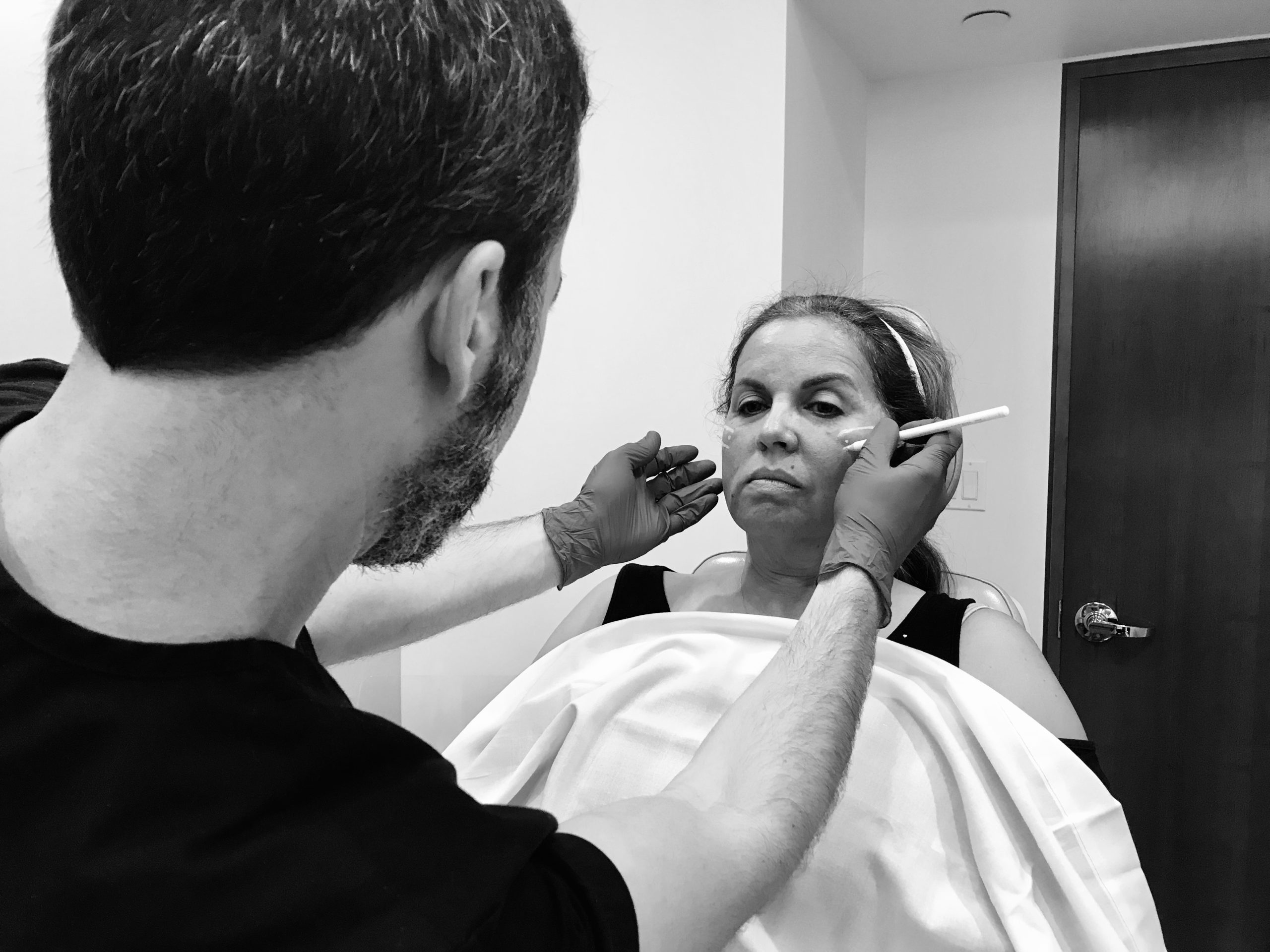 Dr. Jason Champagne marking facelift treatment areas on a patient during consultation